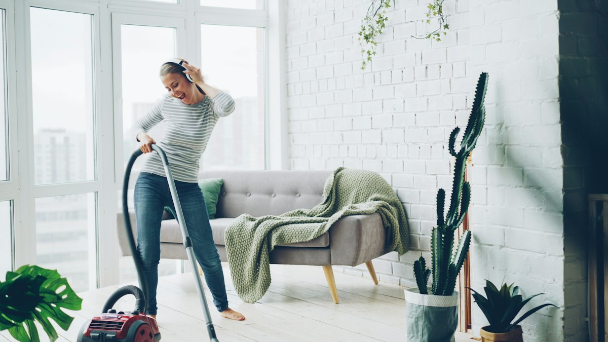 Someone vacuuming a bright loft living room with the music on, plants and a soft green throw on the sofa